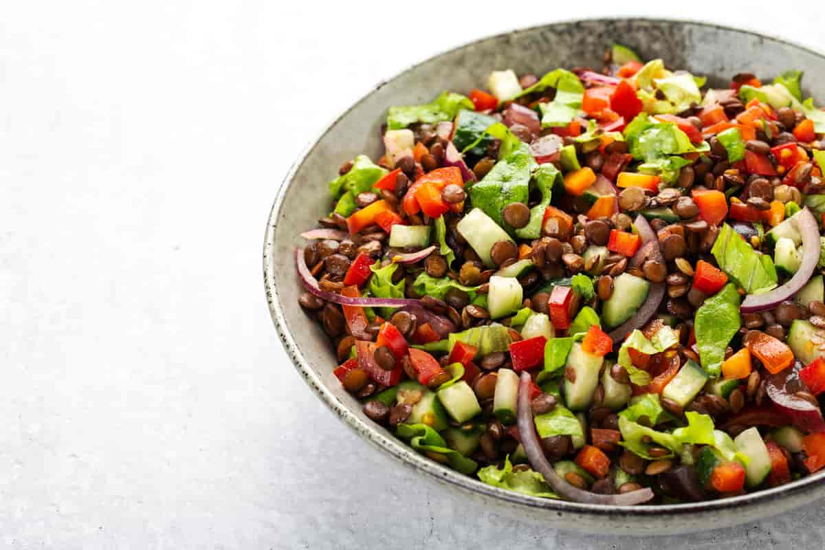 Skål med salat, linser, agurk, paprika og lauk. 