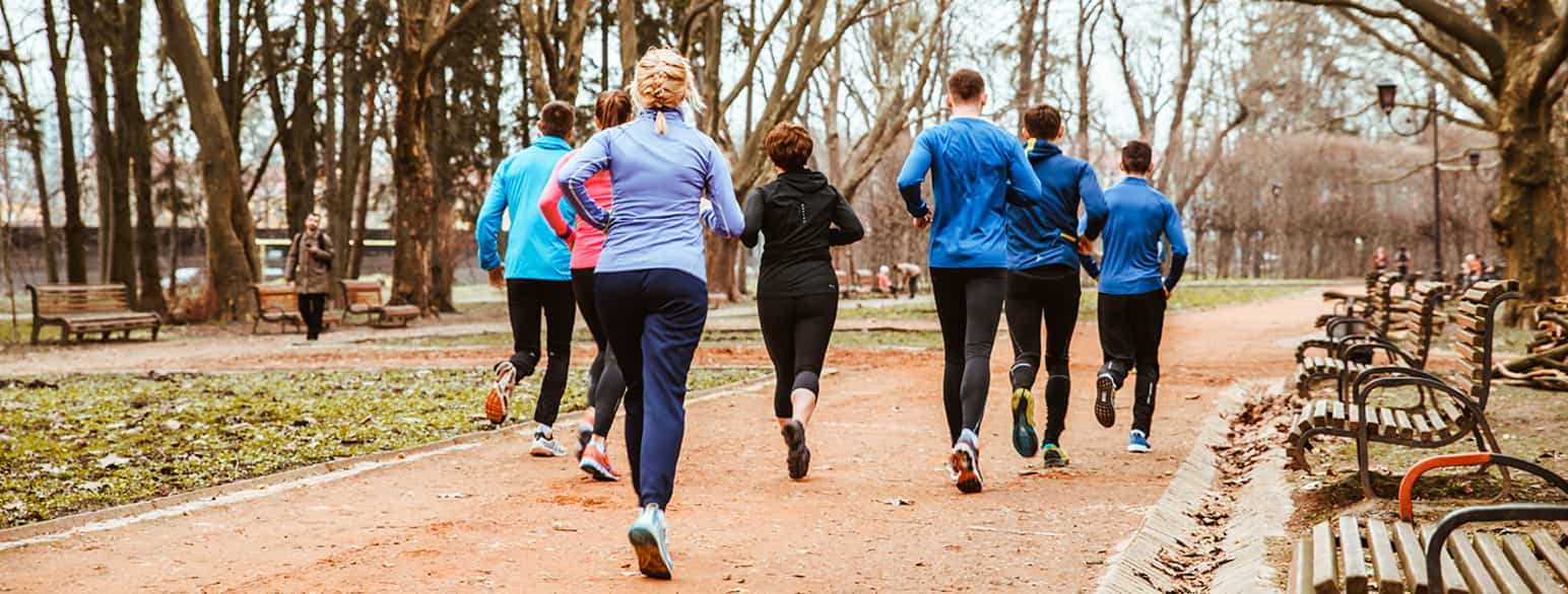 Foto av en gruppe mennesker som jogger i en park på en grussti, sett bakfra.