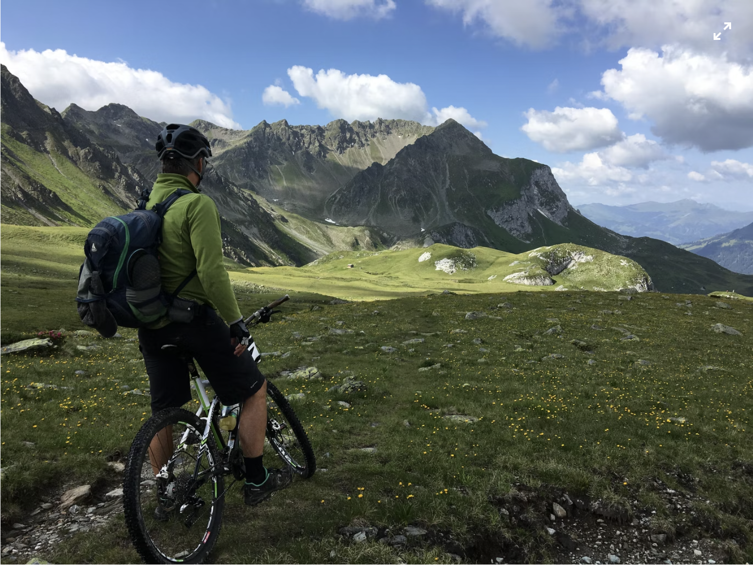 A man holding up a bicycle overlooking mountains in Switzerland