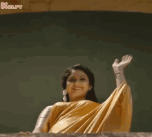 a woman in a yellow saree is waving her hand