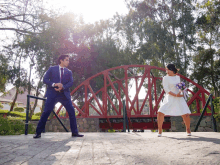 a man in a blue suit and a woman in a white dress are standing in front of a red bridge