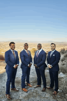 four men in suits and ties are standing next to each other on a hill .