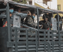 a group of soldiers are riding in the back of a truck and one is pointing a gun