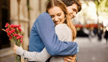 a man is hugging a woman while holding a bouquet of flowers .