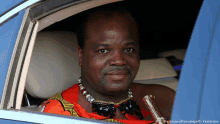 a man is sitting in a car wearing a necklace and looking out the window