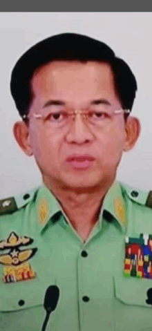 a man in a green military uniform stands in front of a microphone and has a medal on his chest