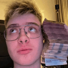 a man wearing glasses holds a stack of 1000 ukrainian hryvnia bills