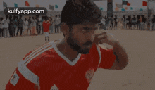 a man in a red and white soccer jersey is standing on a field with a crowd behind him .