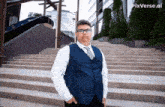 a man in a blue vest and white shirt stands on a set of stairs with pixverse.ai in the corner