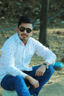 a man wearing sunglasses and a white shirt sits on a concrete block