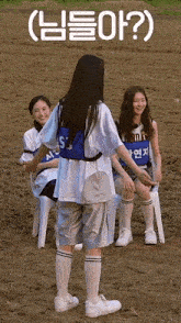 a group of girls are sitting in chairs in a field and one of them is standing in the dirt .