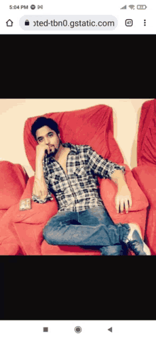 a man in a plaid shirt is sitting on a red couch with his hand on his chin