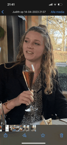 a phone screen shows a woman holding a glass of wine and the date 14-04-2023