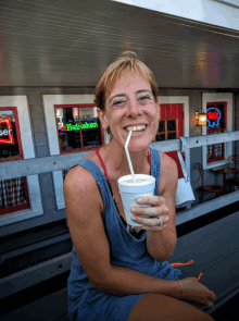 a woman drinking a milkshake with a straw in front of a heineken sign