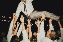 a man in a white shirt and tie is being lifted in the air by his friends