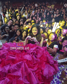 a woman in a pink dress stands in front of a crowd with a sign that says chikkaness ave on it