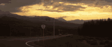 a sunset over a road with mountains in the background and a white sign that says " no left turns "