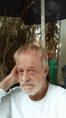 a man with a beard and a white shirt holds his hand to his head