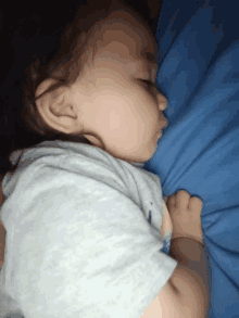 a baby sleeping on a blue blanket with a gray shirt on