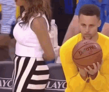 a man in a yellow shirt is holding a basketball in his hands while a woman stands behind him .