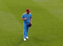 a baseball player wearing a blue uniform and a red hat is walking on the field .