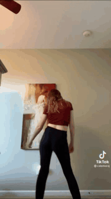 a woman in a red top and black pants is dancing in front of a mirror