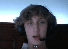 a young man wearing headphones and a microphone looks at the camera with a skype icon in the corner