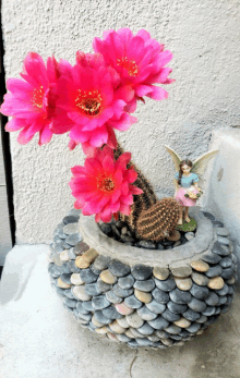 a fairy figurine sits next to a cactus in a rock planter