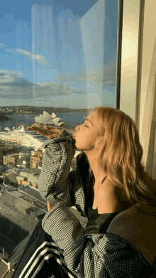 a woman blows a kiss while looking out a window at the sydney opera house