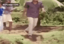 a man in a blue shirt and white pants is walking through a field with a group of people .