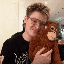 a young man wearing glasses is holding a stuffed monkey in his hands .