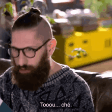 a man with a beard and glasses is sitting on a couch and says tooou che .