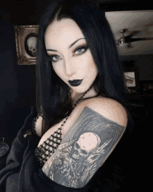 a woman with long black hair and a tattoo of a skull on her arm is standing in a dark room .