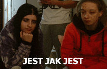 two girls are sitting in front of a sign that says jest jak jest on it