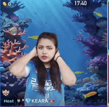 a girl in a blue shirt is standing in front of a coral reef and the time is 17:40