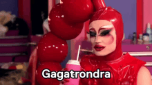 a drag queen in a red latex costume is holding a pink cup with a straw and says gagatrondra .