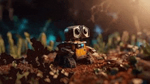 a small wall e robot is sitting on top of a pile of dirt .