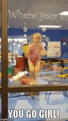 a little girl is jumping on a balance beam in a gym with the words " you go girl " below her