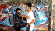 two young men are standing in front of a wall that has graffiti on it including one that says ' oars '