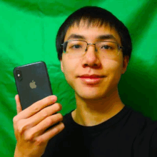 a young man wearing glasses is holding an apple iphone in front of a green background