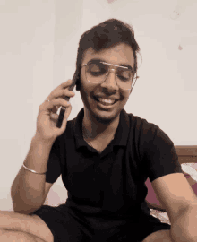 a young man wearing glasses and a black shirt is talking on a cell phone