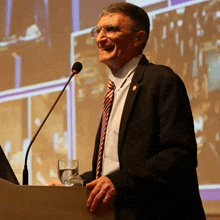 a man in a suit and tie stands at a podium with a glass of water in front of him