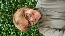 a woman wearing glasses is smiling in front of a wall of green leaves