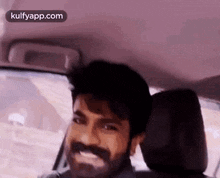 a man with a beard is sitting in the driver 's seat of a car and smiling .