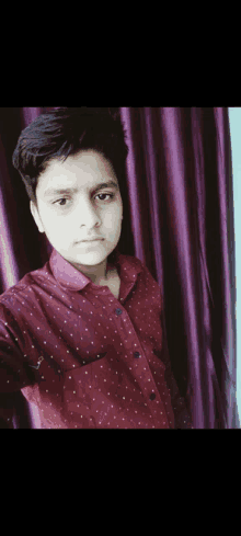 a young boy wearing a red shirt with white polka dots poses for a picture