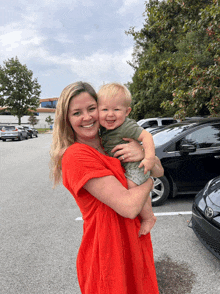 a woman in a red dress is holding a smiling baby