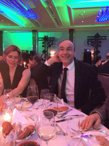 a man in a suit sits at a table with wine glasses