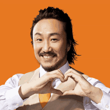 a man making a heart shape with his hands on an orange background