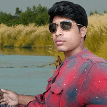 a young man wearing sunglasses stands in front of a body of water