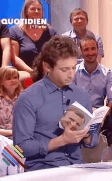 a man in a blue shirt is reading a book in front of a group of people with the word quotidien on the bottom right